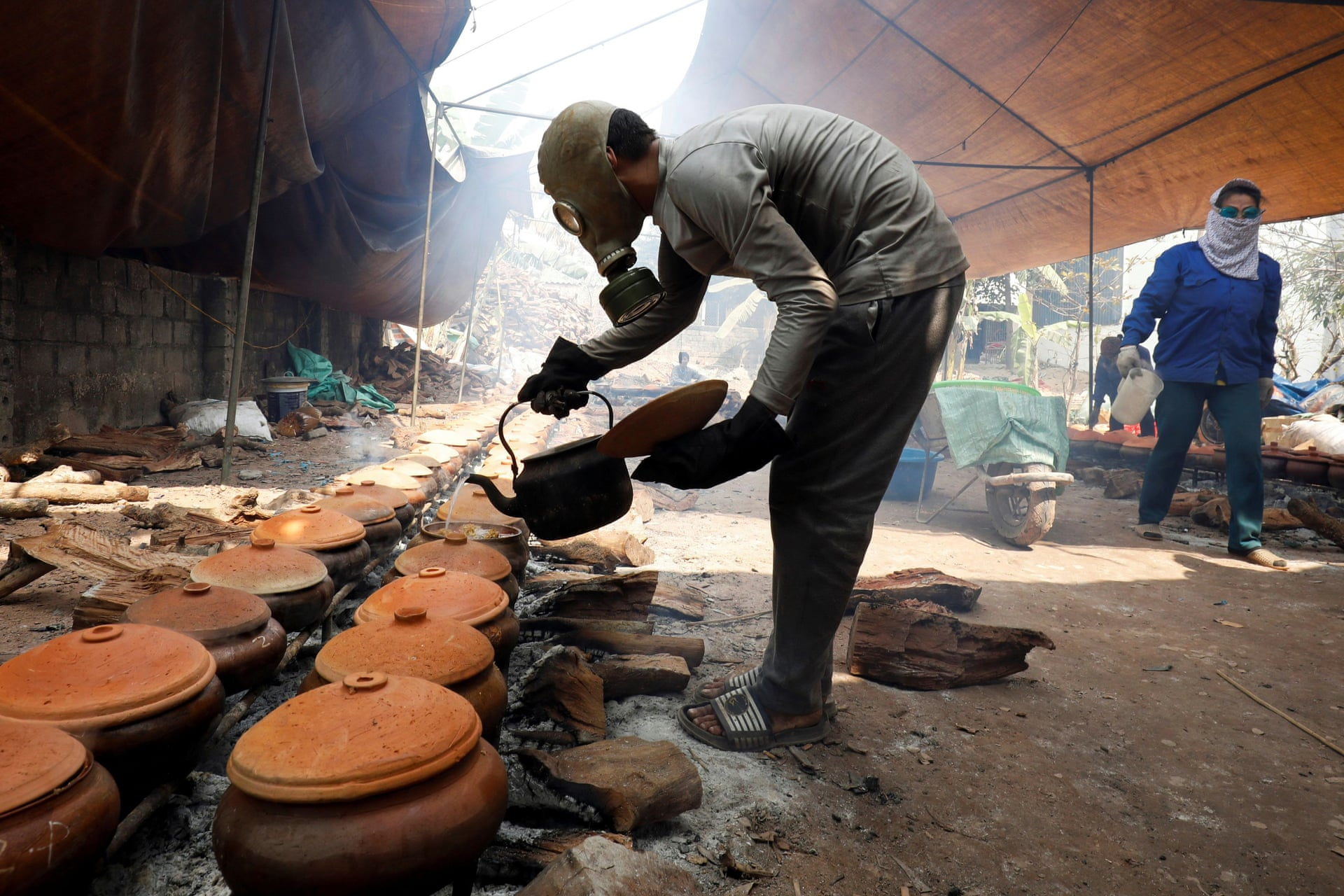 A man wears a gas mask as he braises black carp in clay pots with firewood to serve as a traditional Vietnamese dish, Ha Nam Province. Photo by Reuters/Kham. 2748 1 1613359647 1613462325 3267 1613462457