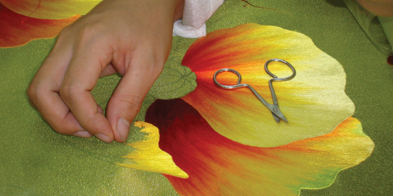 Embroidered peonies in process at the XQ Center in Huê, Vietnam. Note at bottom the outlines in stem stitch and the groundwork fill-in stitches in pale pink at top. Both of these are preliminary steps to the final embroidery. Unless otherwise noted, all photographs by Cynthia LeCount Samaké. 3114-embroiderers-at-the-xq-center-in-hue-vietnam