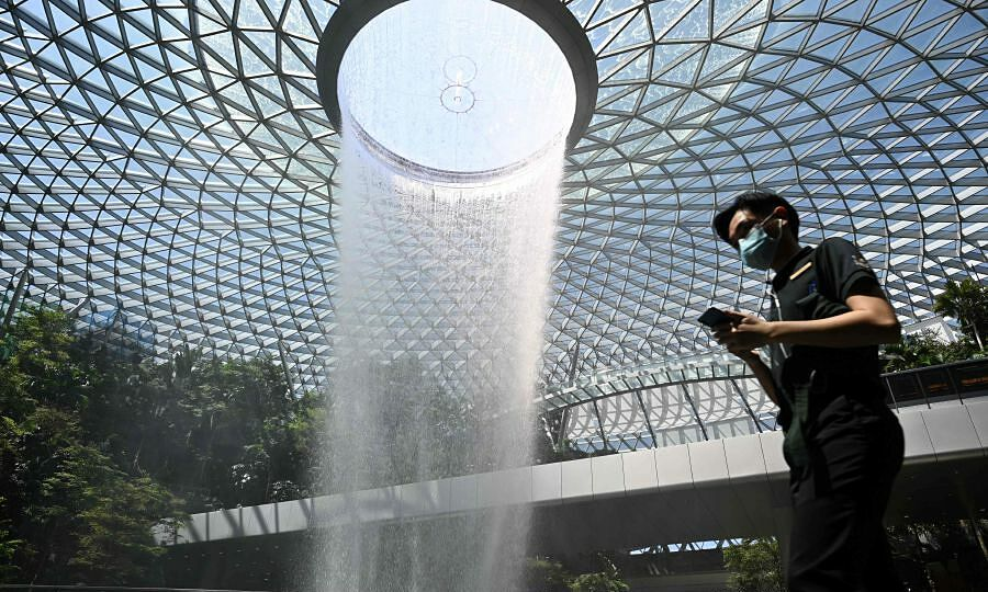 A man, wearing a protective facemask, walks past the Rain Vortex display at Jewel Changi Airport in Singapore on February 27, 2020. Photo by AFP/Roslan Rahman. 4915 singapore 2